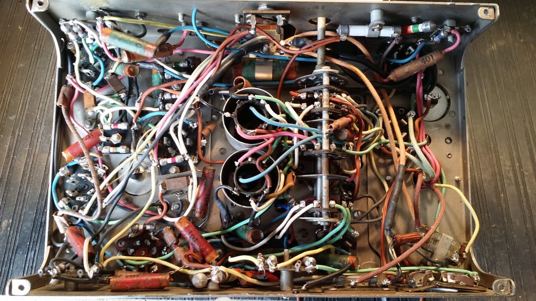 The underside of a metal radio chassis exposing a tangled, chaotic network of colorful electrical wires, capacitors, and soldered hardware joints.