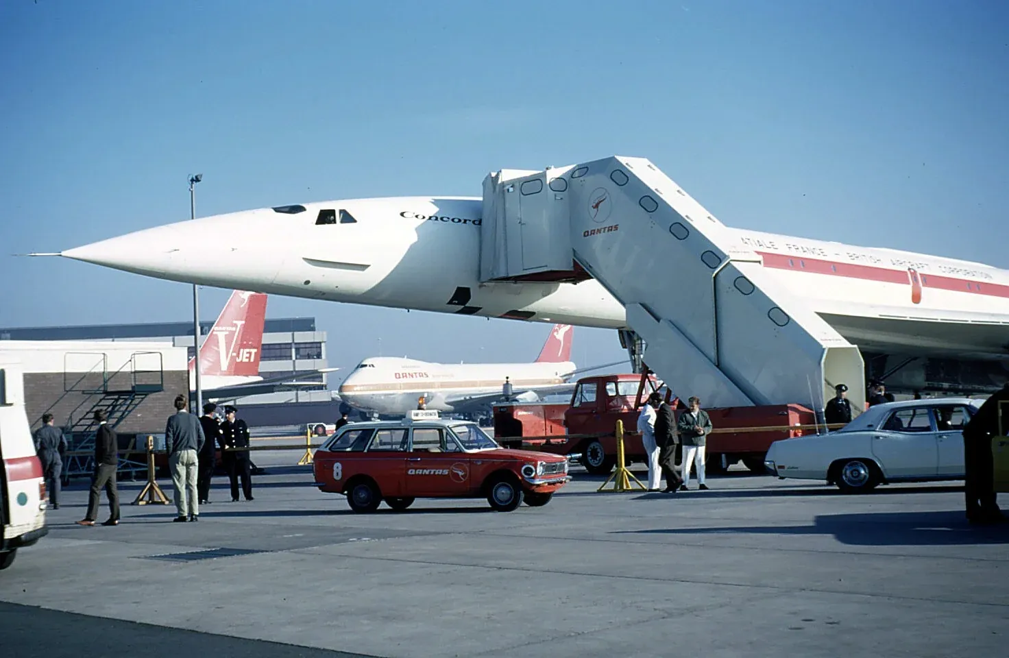 A sleek white Concorde airplane prototype on the tarmac, surrounded by Qantas vehicles, a symbol of high-speed globalized accumulation.