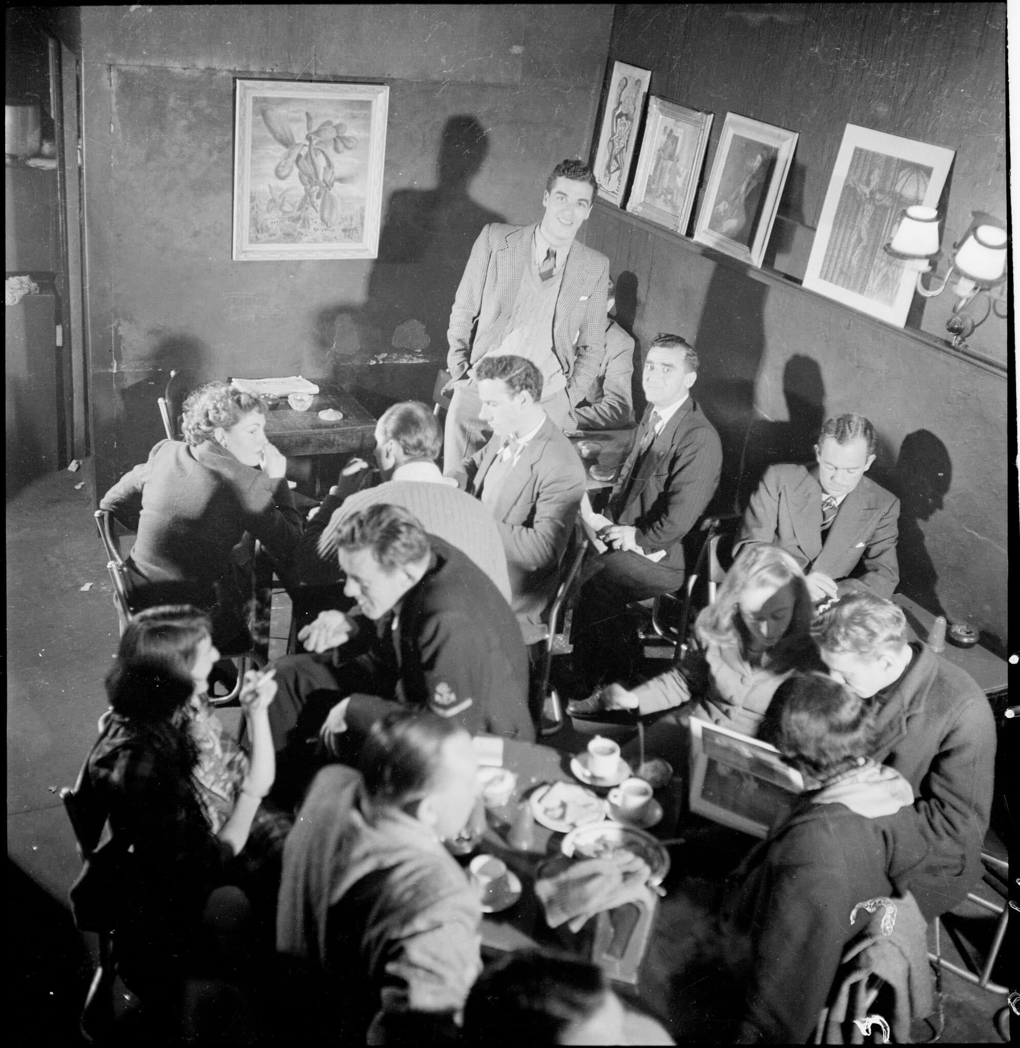 Black and white photo of intellectuals smoking and conversing in a crowded coffee lounge, theorizing abstractly while the class war rages outside.
