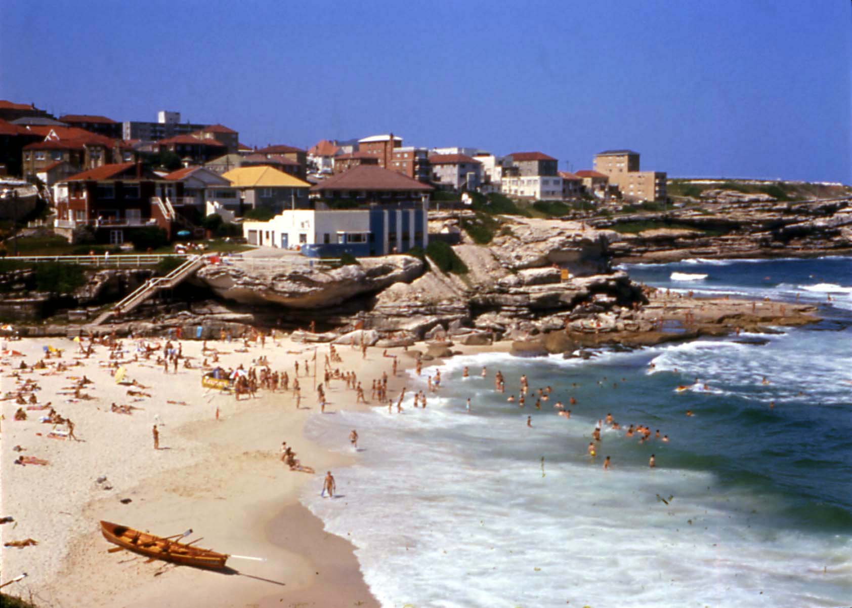 Crowds of people sunbathing and swimming at Tamarama Beach, structurally contained within designated recreational zones.