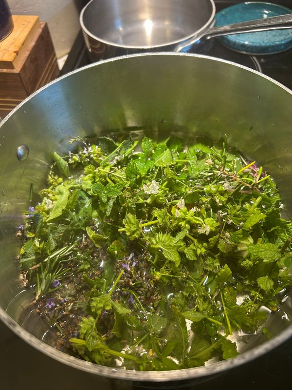 Photo of a stainless steel pan on the stove full of chopped green herbs such as lemon balm, rosemary, basil, and catmint
