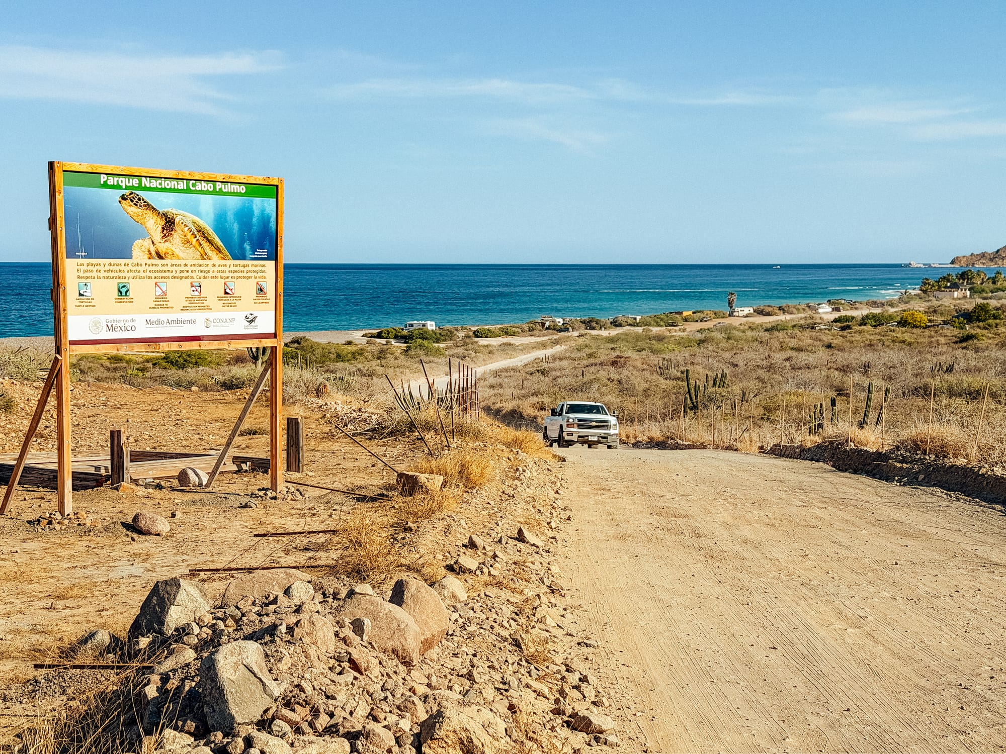 Strada sterrata nel deserto con il cartello in legno che segna l'ingresso al Parco Nazionale Cabo Pulmo.