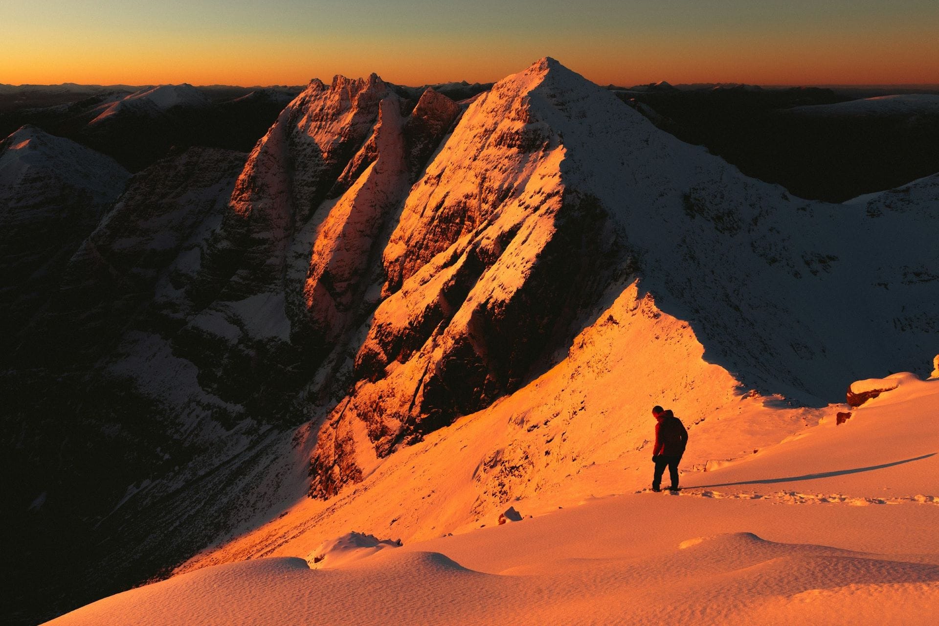 Alpinista osserva il vuoto da una parete innevata illuminata dalla luce del tramonto, affrontando la fatica estrema della pratica misogi.