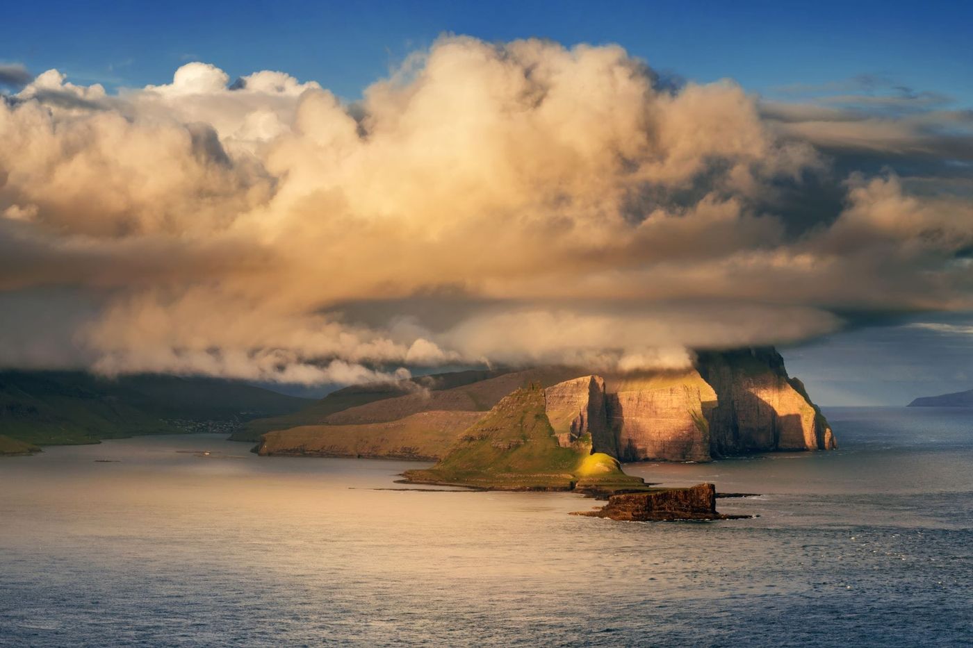 Scogliere illuminate dal sole sotto una grande nuvola sul mare delle isole Faroe, con isole all'orizzonte