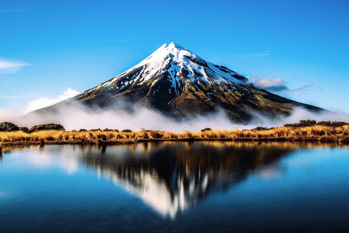 Il vulcano Taranaki innevato riflesso nei Pouakai Tarns, in Nuova Zelanda, con nebbia e prati di tussock