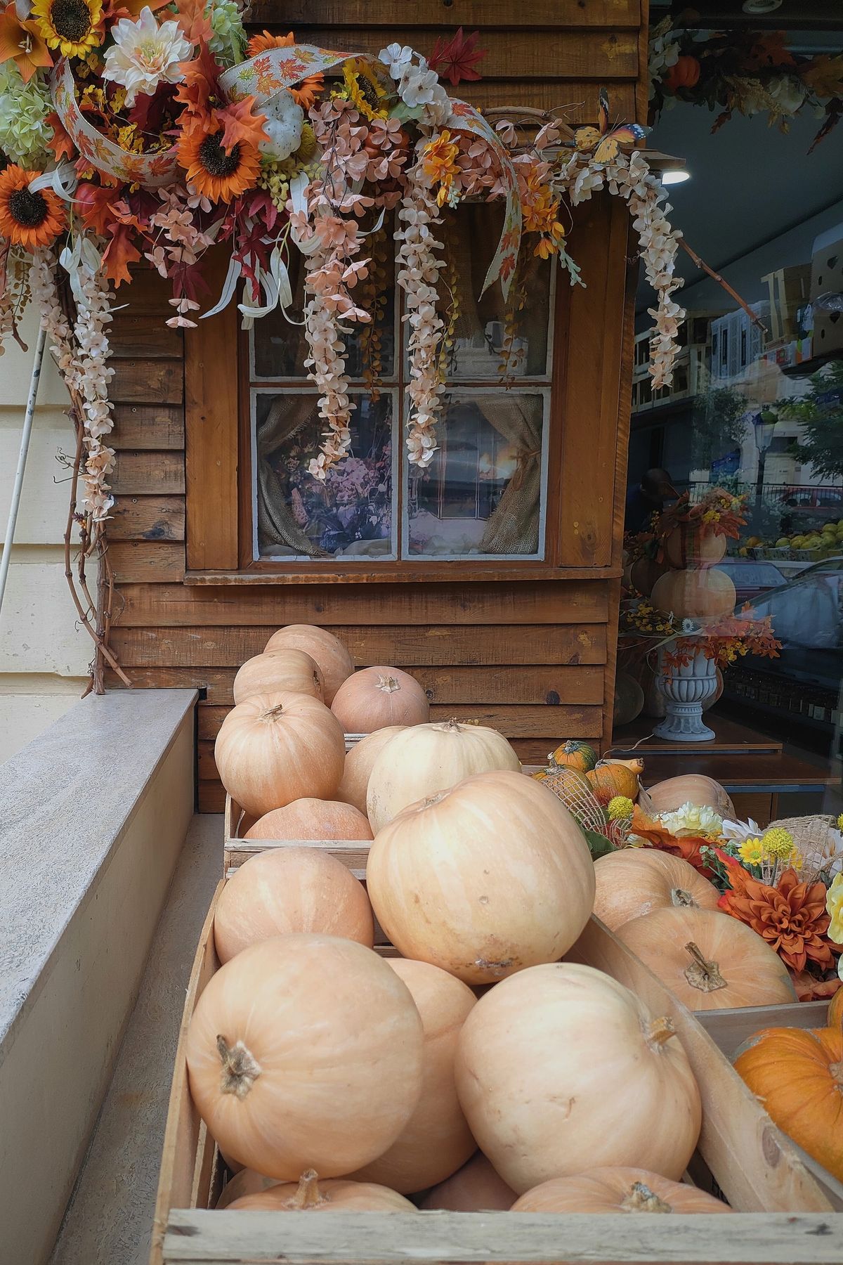 la entrada de una tienda con decoraciones otoñales de gerberas color naranja en una guirnalda y cestos de madera repletos de calabazas grandes