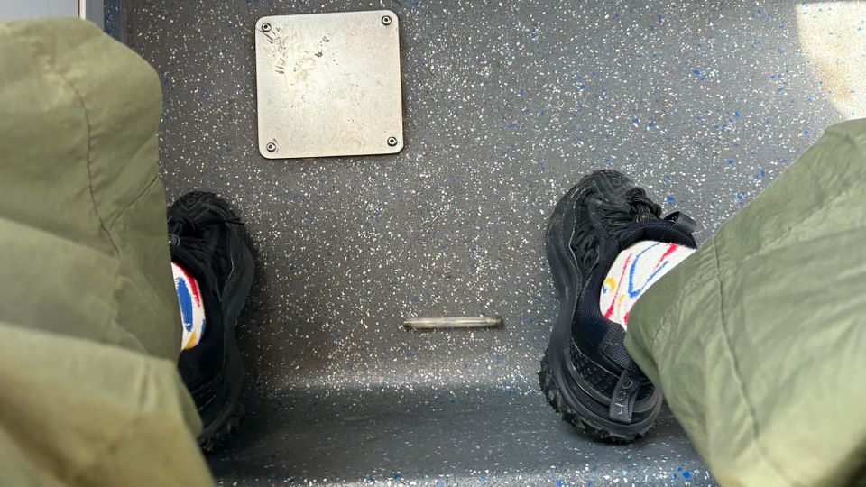 Small glass pipe with burnt ends (makeshift crack pipe) laying on grey bus floor, in between writer's feet (wearing black rubber shoes)