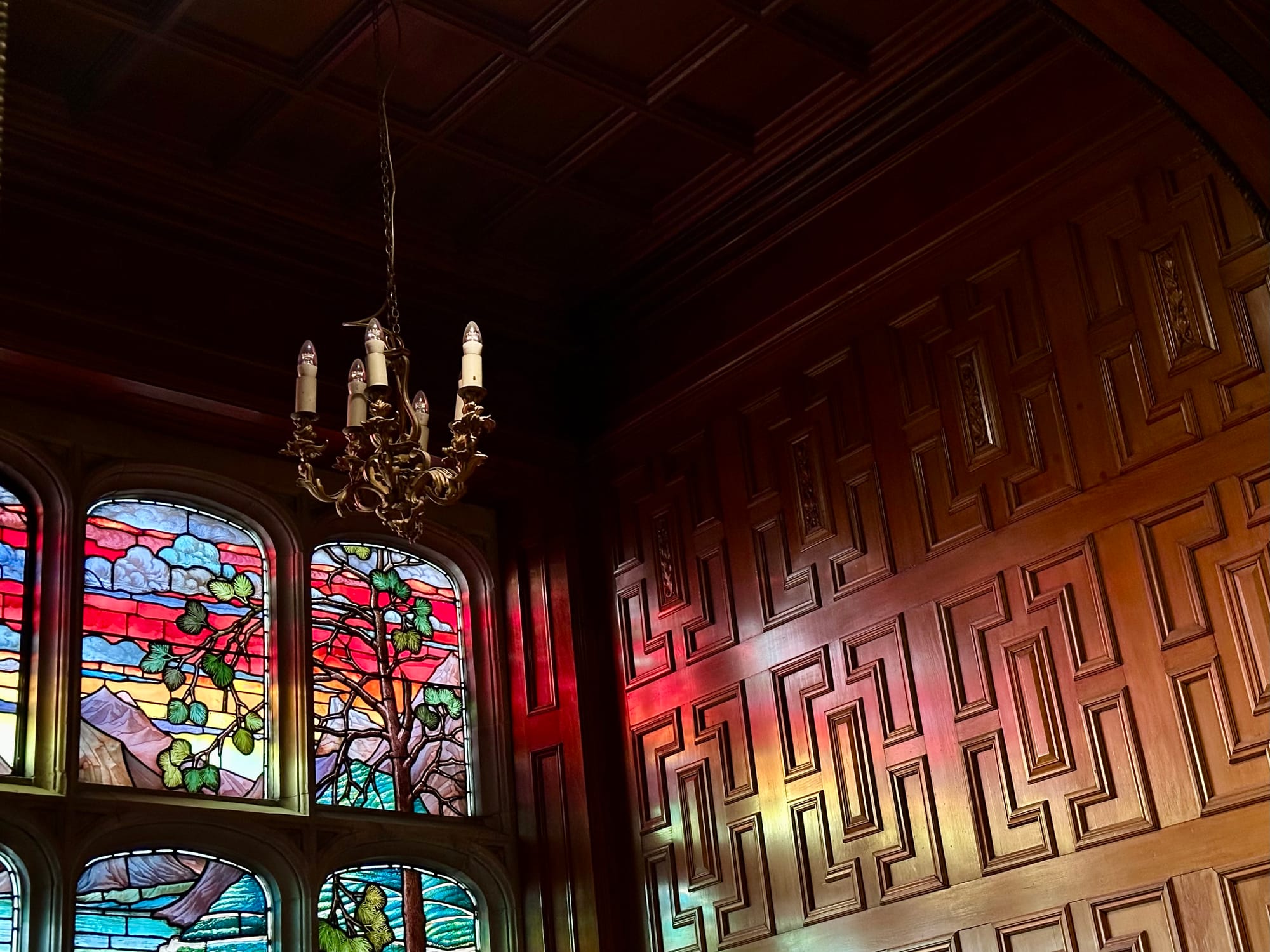 Stain glass window throwing reddish-pink light onto an ornately panelled timber wall.