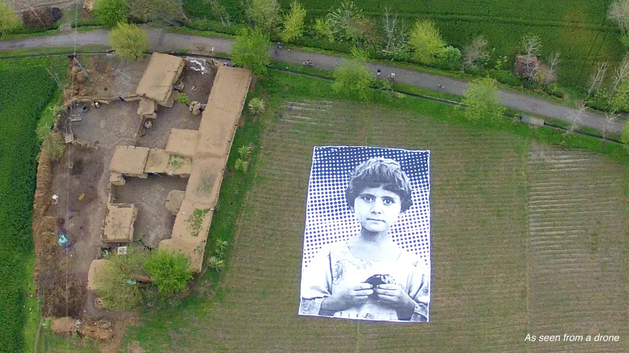 #NotABugSplat a large than life photographed aerially by a drone showing the portrait of a young child rot highlight civilian collateral damage of automated warfare.