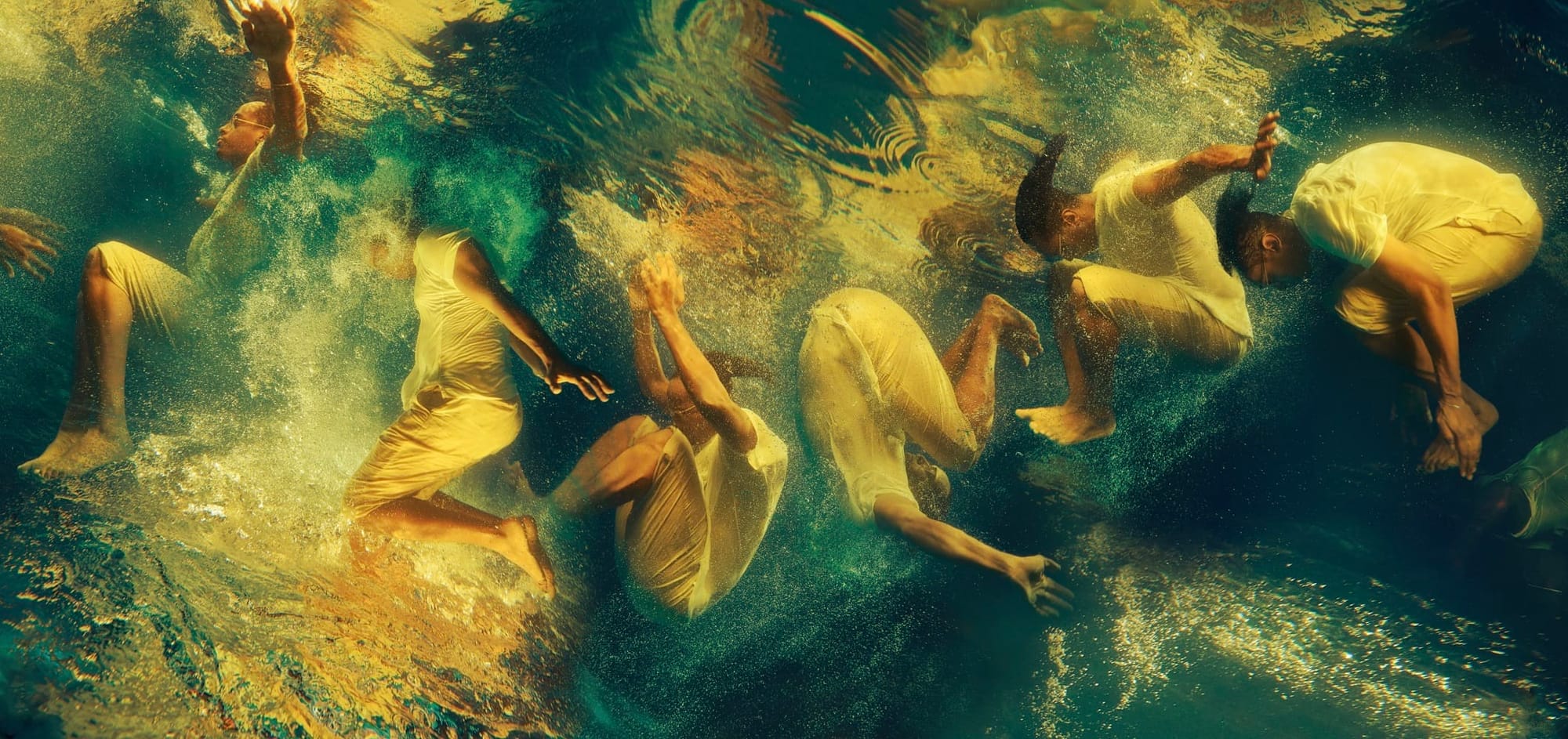 Photo of an art installation by the side of the escalator in a London Underground station, showing various people of Black, African, and Caribbean heritage immersed underwater and dressed in white.