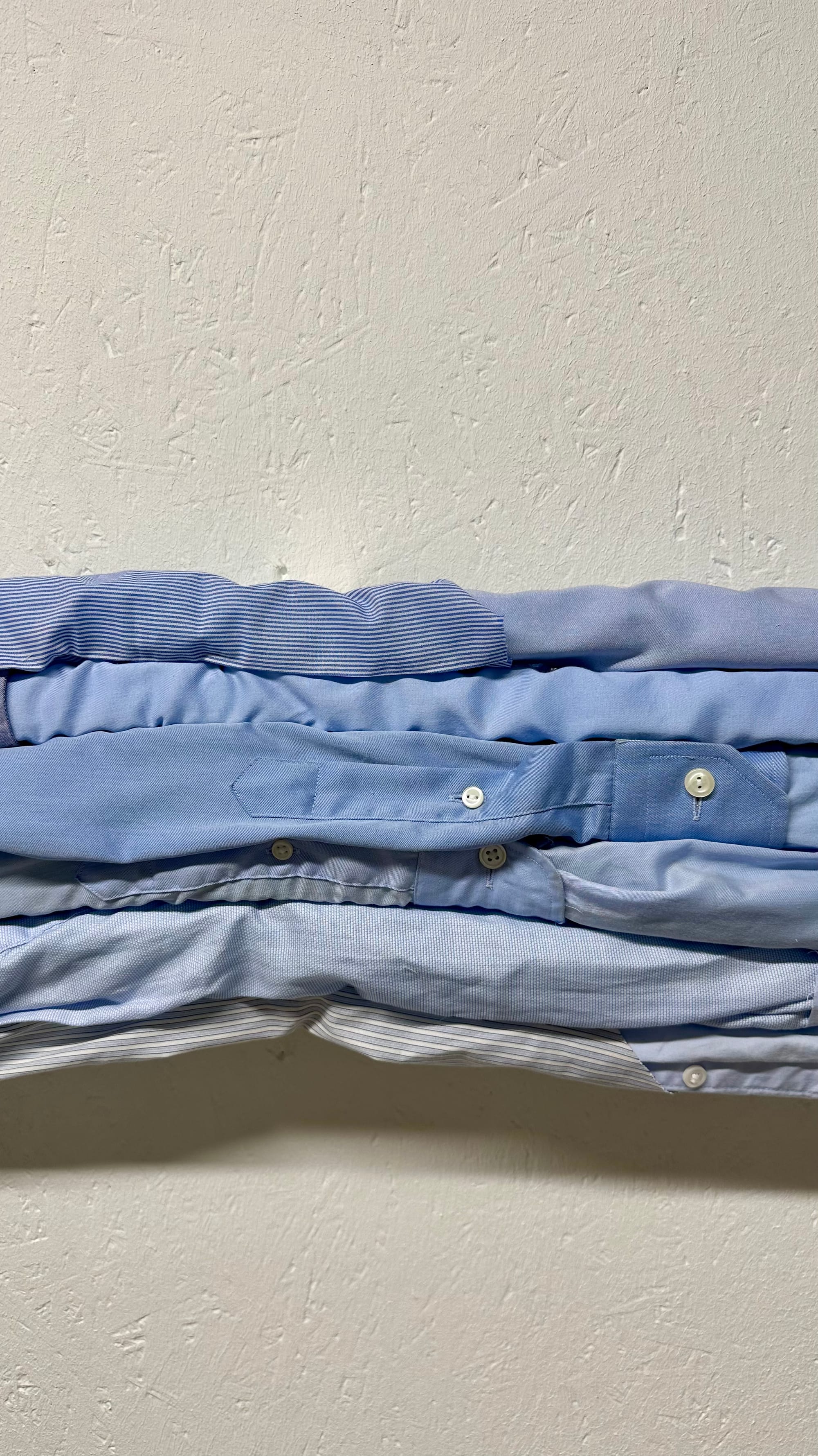 Six blue cotton shirt sleeves arranged in horizontal layers as art of an artwork.