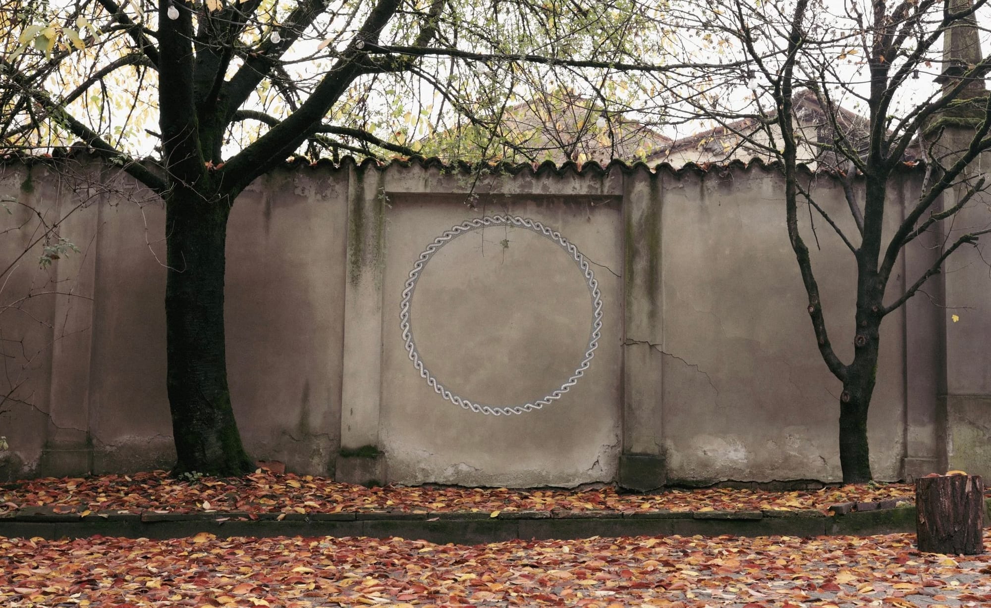 Ornate braided circle mural painted on a wall in an autumnal garden.