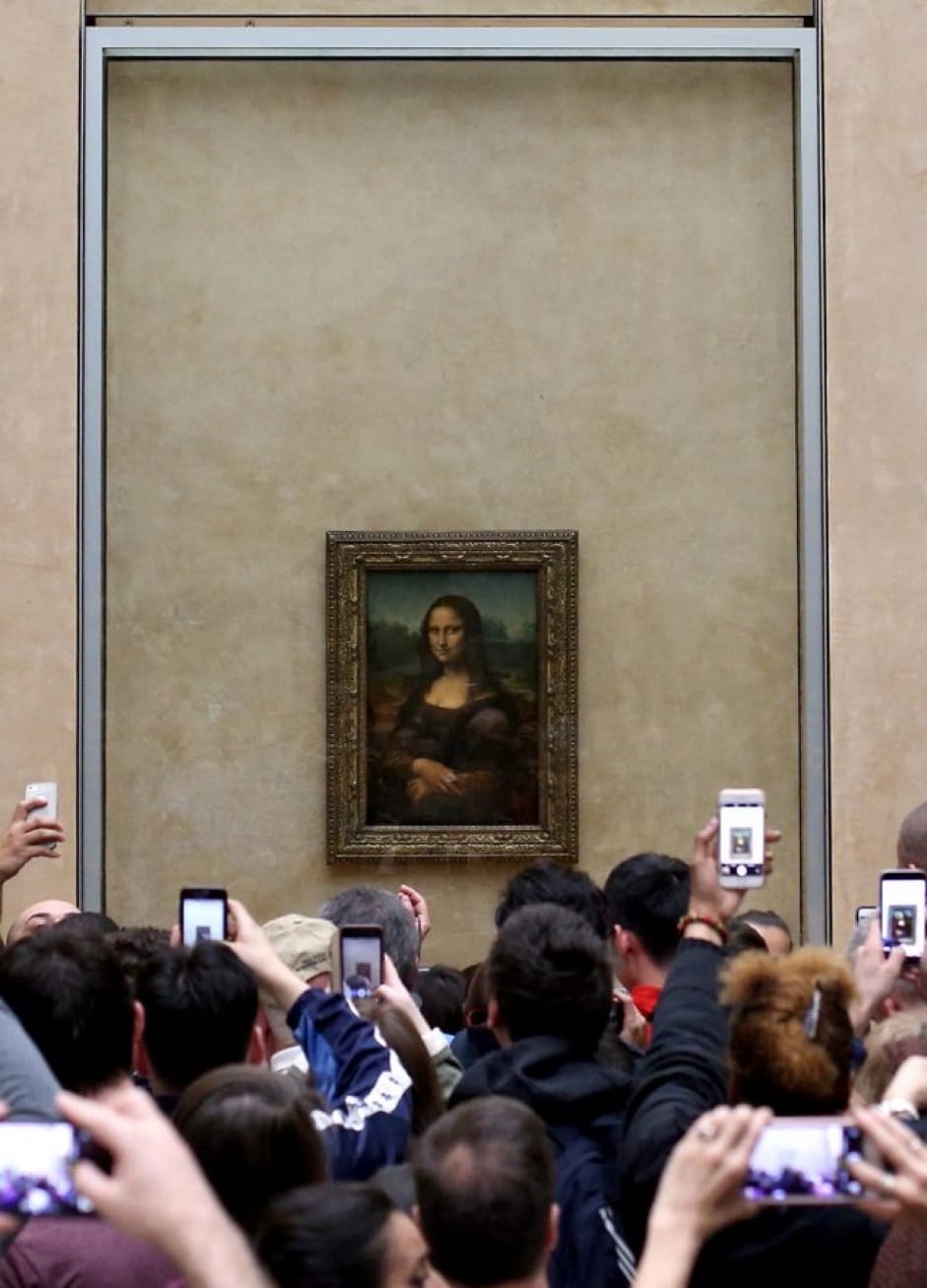 Photo of crowds in front of the Mona Lisa in the Louvre who are all straining to take photos of the Mona Lisa.