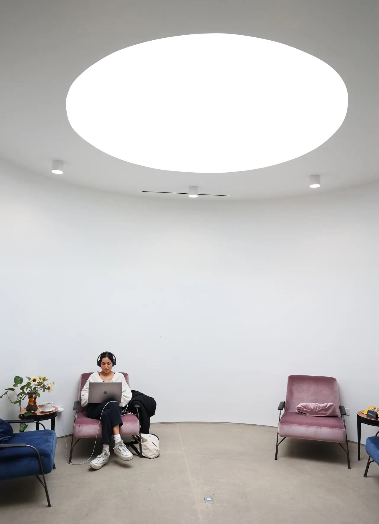 Unknown woman sitting in a coffee shop (or maybe gallery) with white walls under a circular skylight.