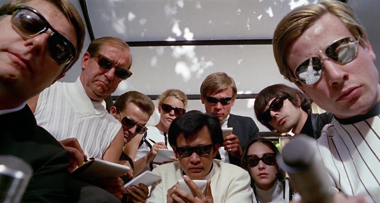Still from La Decima Vittima, showing multiple reporters looking into the camera as if the viewer is on the ground underneath them.