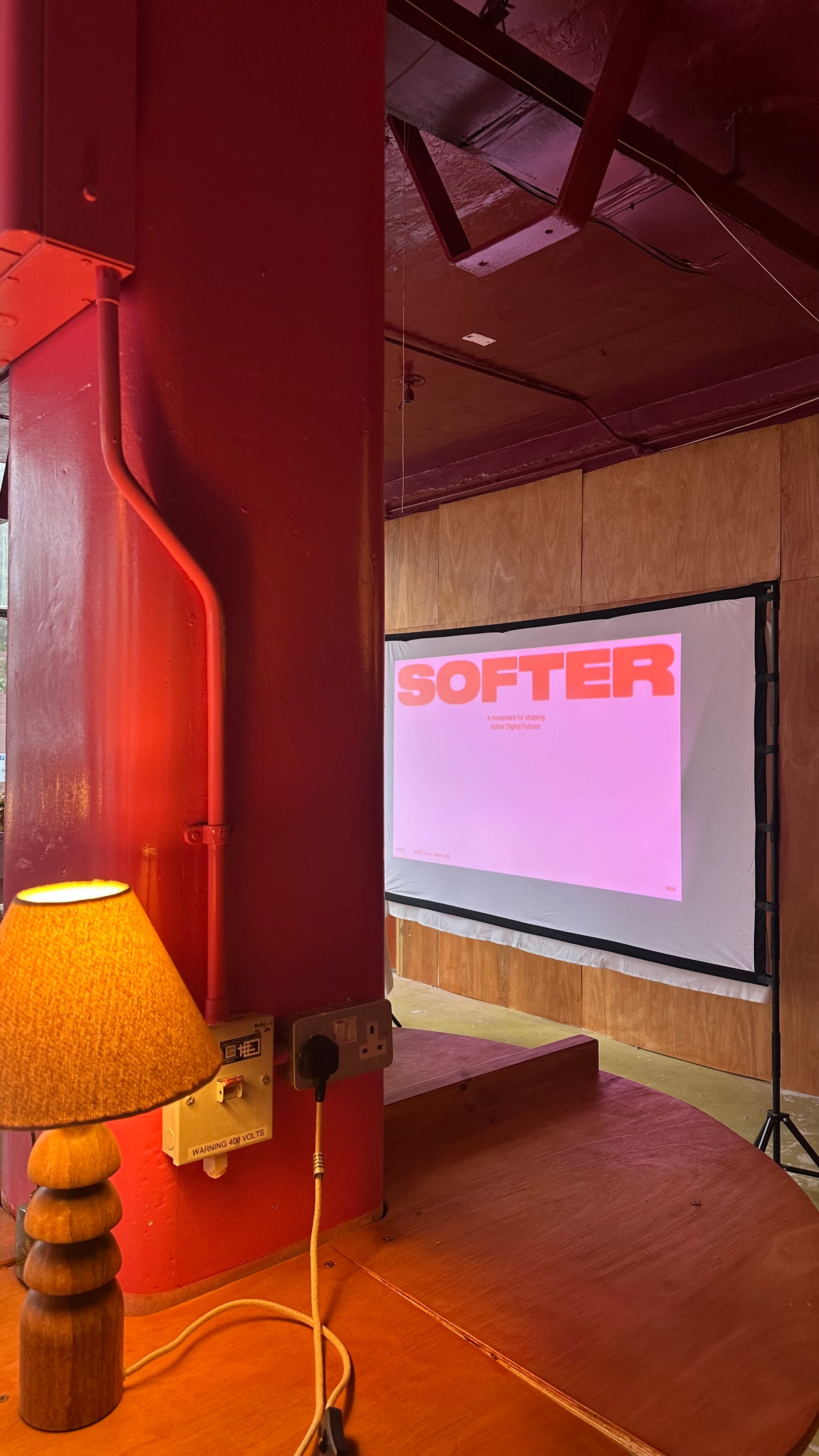 Photo of Softer Digital Futures logo on a projector screen in an exhibition space with lovely pink and red walls.