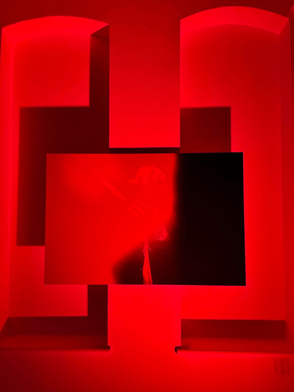 A photo of an obscure black and white photo mounted on an alcoved wall bathed in red light.