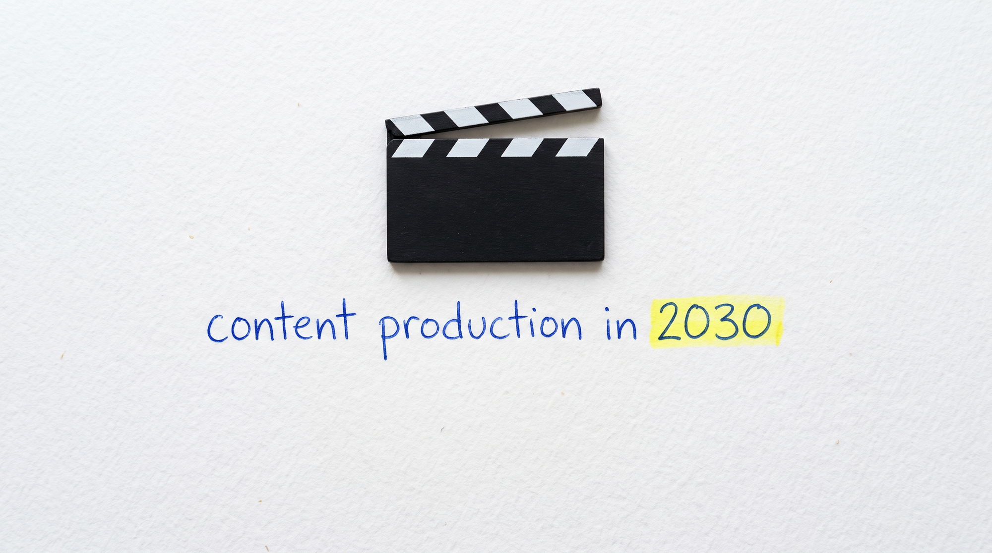 Handwritten blue pen on white paper reading "content production in 2030", with the year highlighted in yellow and a small clapperboard lying flat above it