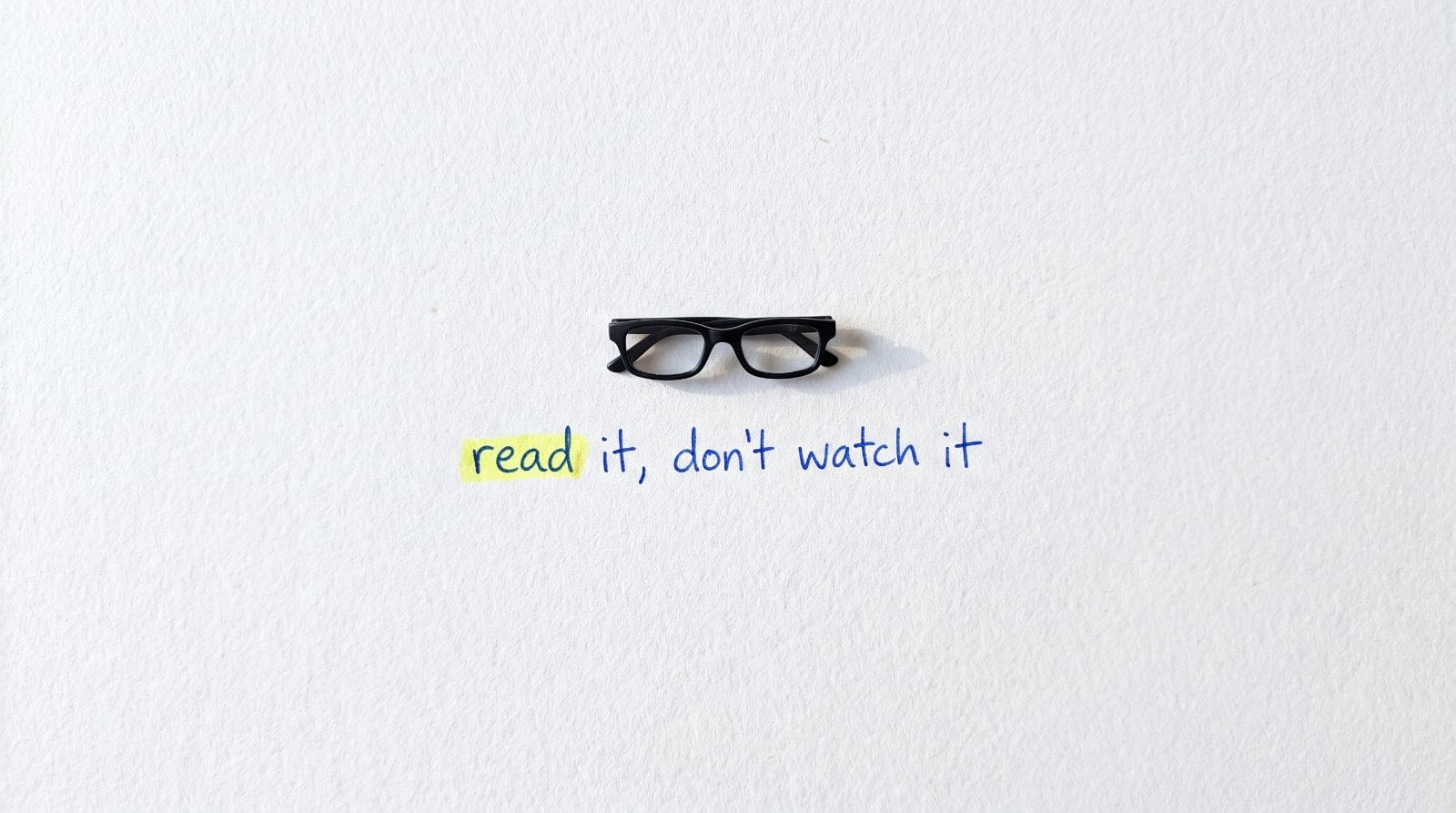 Black reading glasses on white paper with the handwritten words: read it, don't watch it. The word read is highlighted.