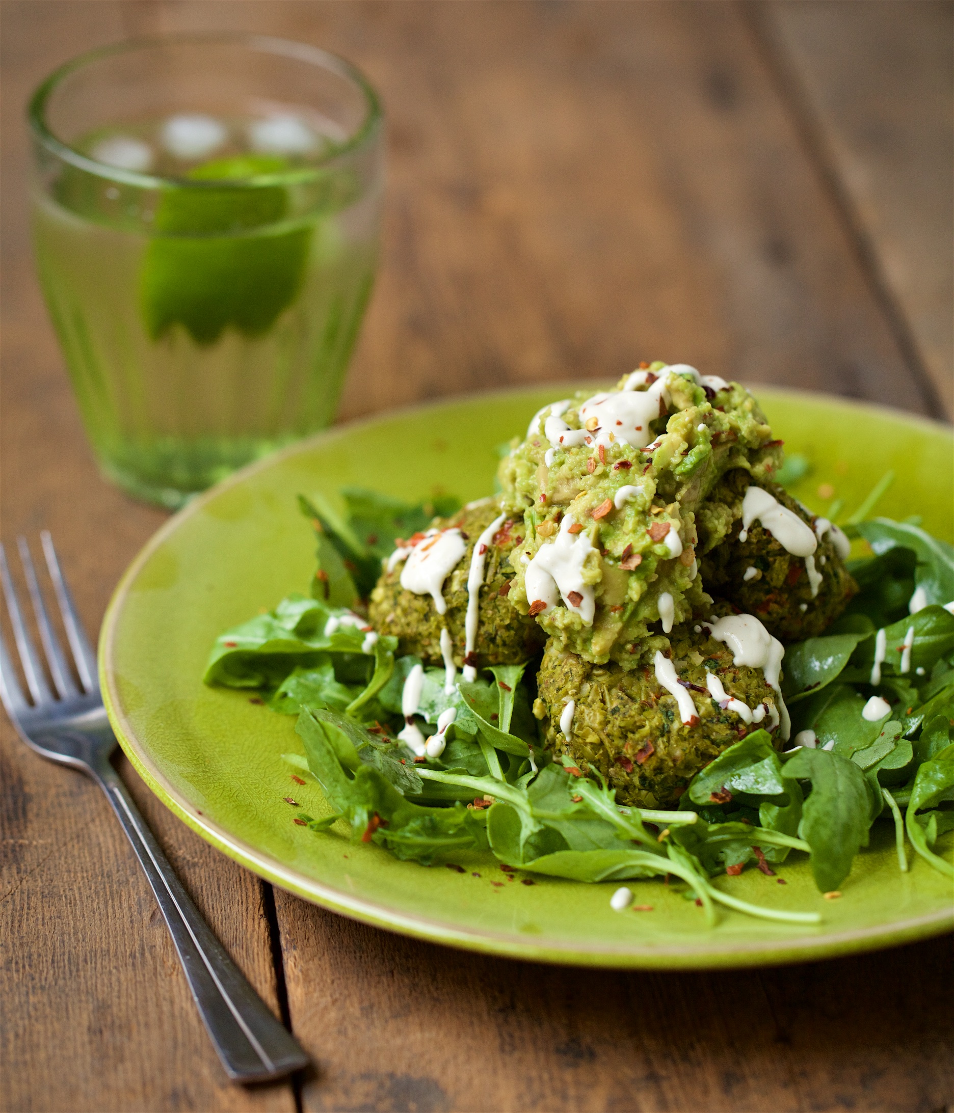 Pea and mint croquettes with guacamole and cashew sour cream on spinach on green plate