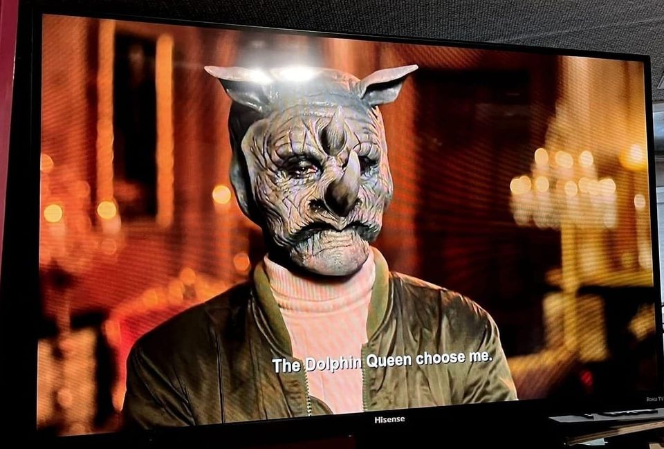 A TV screenshot of man with his face covered in rhinoceros makeup stands in a room filled with lit candles, and the caption, “The Dolphin Queen chose me.”