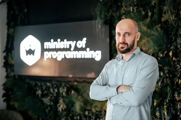 Product manager standing confidently in front of the Ministry of Programming logo in a modern office setting.