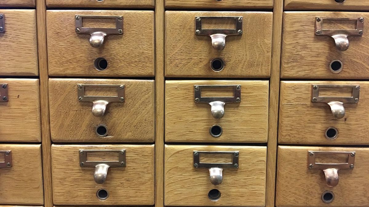 Rows of closed wooden card catalog drawers with empty brass label holders.