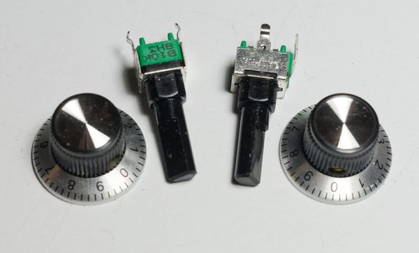 Two black and silver control knobs with numbered dial skirts from 0 to 9, lying beside two loose potentiometers on a white surface.