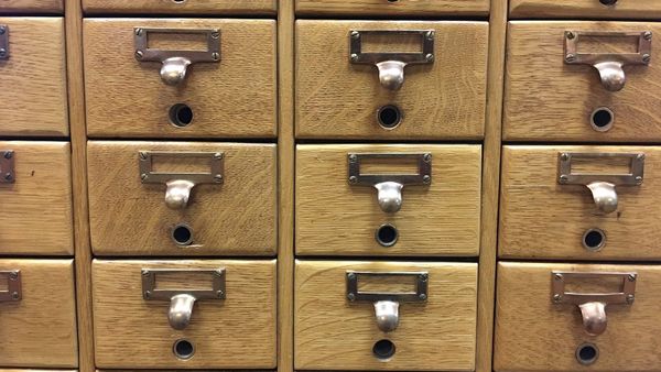 Rows of closed wooden card catalog drawers with empty brass label holders.