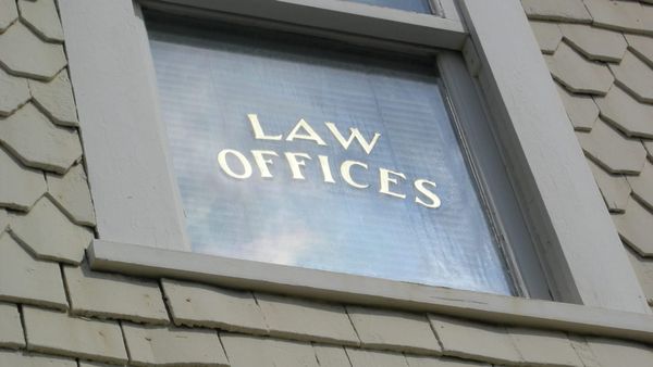Window reading “LAW OFFICES” viewed from below on a shingled building exterior, with blinds partially visible behind the glass.