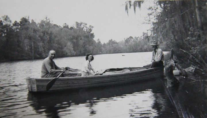 A black and white image from 1944 of two men and a woman in a boat on the water of a bayou 