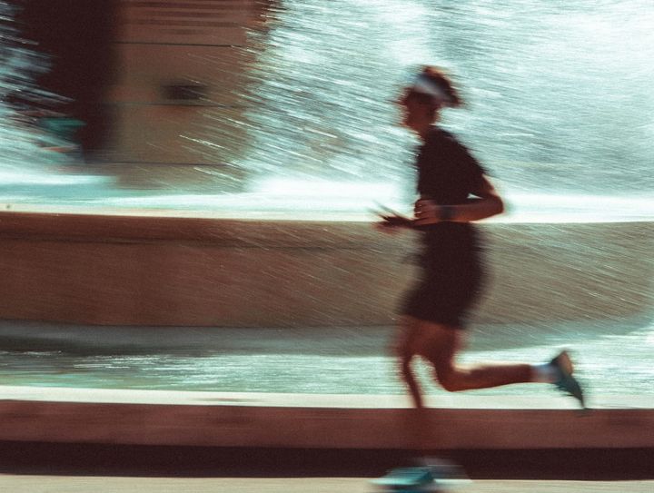 A person running perhaps in a marathon. The backdrop is a fountain and the camera is blurry with movement.