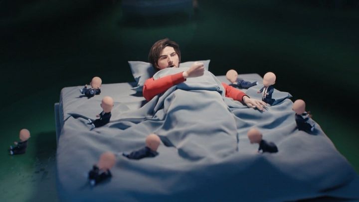 A screenshot from the opening credits of Severance, season 2, from Apple TV showing the protagonist lying on a bed, looking surprised, as numerous faceless babies surround him