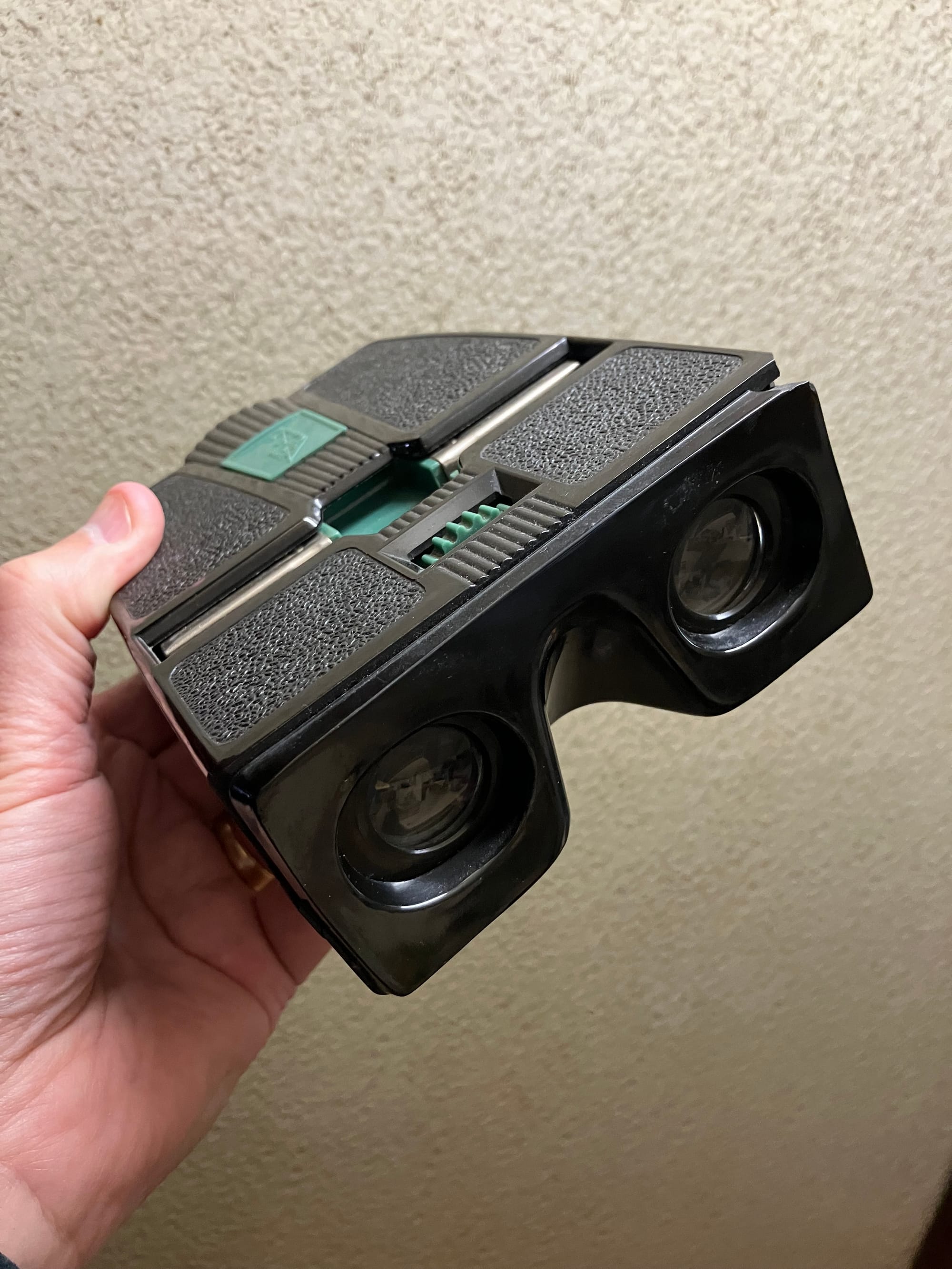 Hand holding up a black stereoviewer with green buttons.