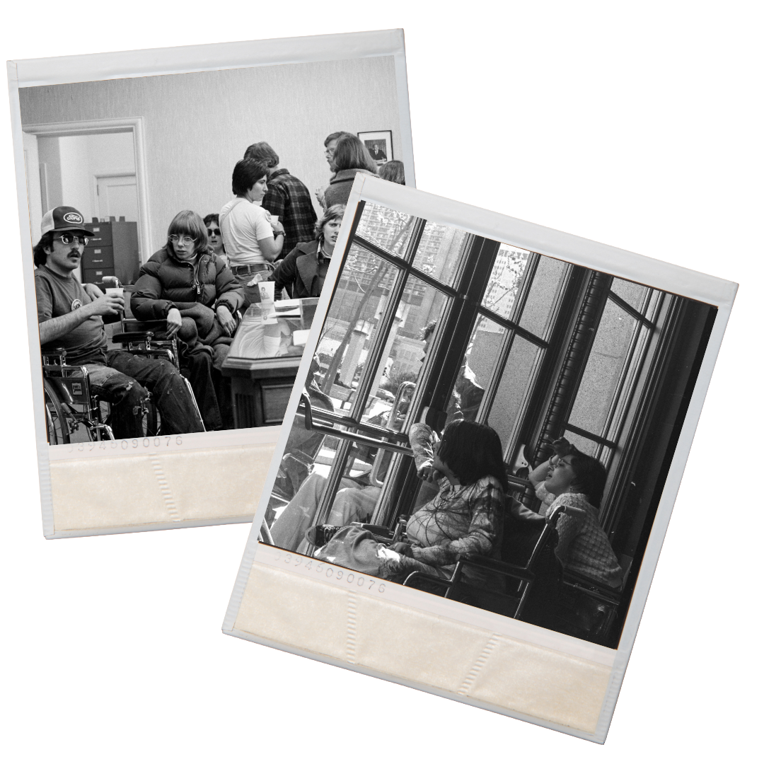 Man in wheelchair wearing a trucker hat and sunglasses sits next to a desk, others in wheelchairs sit around him. People in wheelchairs inside a building looking out of a glass door, where a man with a wheelchair looks in.