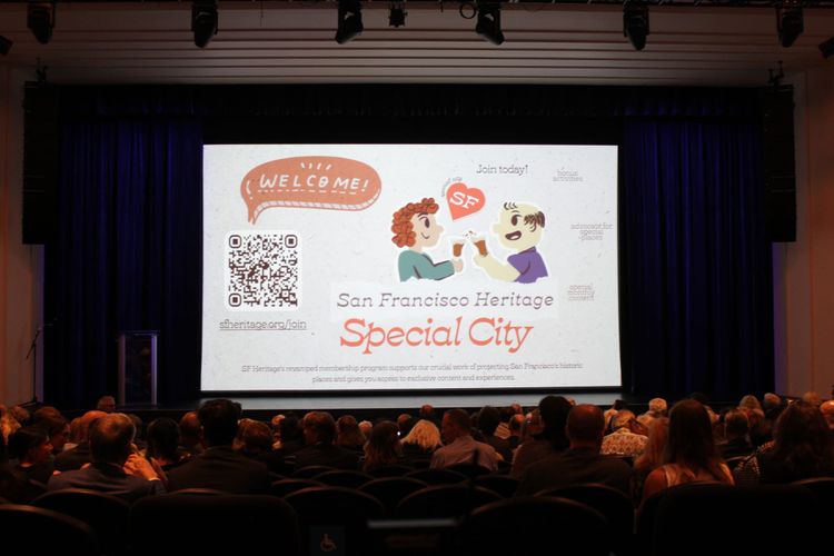 A darkened theater auditorium full of people facing a screen, with ad for "San Francisco Heritage's Special City" and a QR code for sign up.