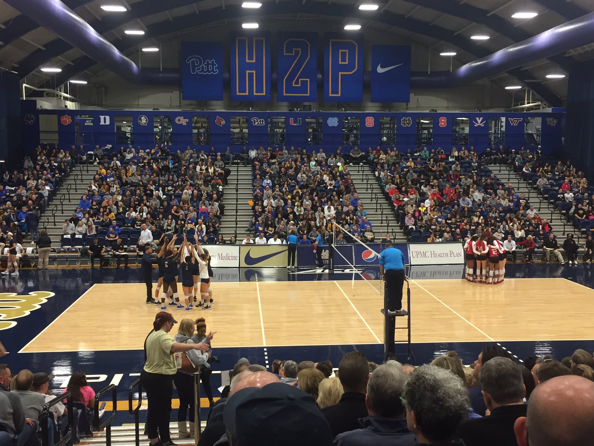 It's a photo of a near-sellout crowd from 2018 at Fitzgerald Field House, and old-fashioned college gymnasium. Pitt is in their darker blue and gold from 2018 on the near side, with Louisville on the far side.