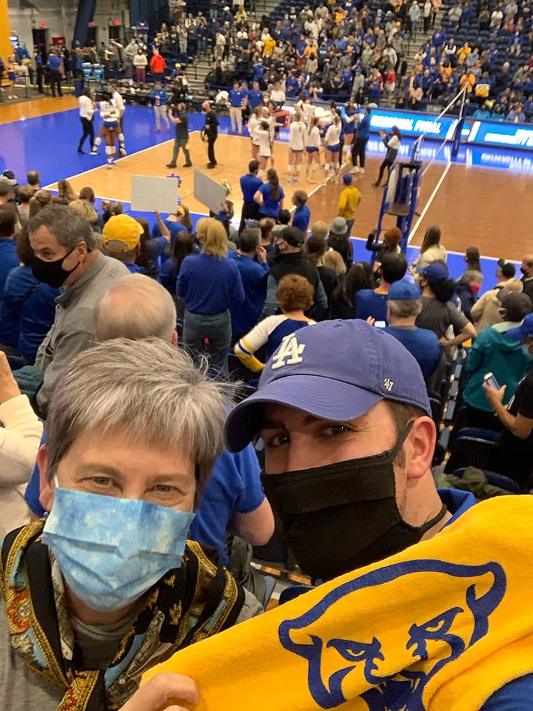 Selfie of James and his mother smiling behind masks as Pitt Volleyball clinches a spot in the Final Four in the background