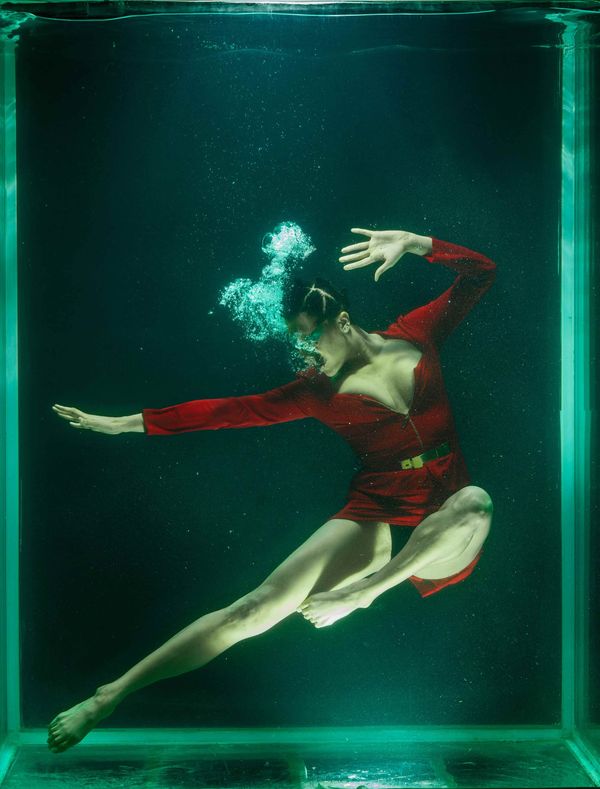 Mujer suspendida bajo el agua con vestido rojo, representando pausa, tensión y decisión antes de actuar
