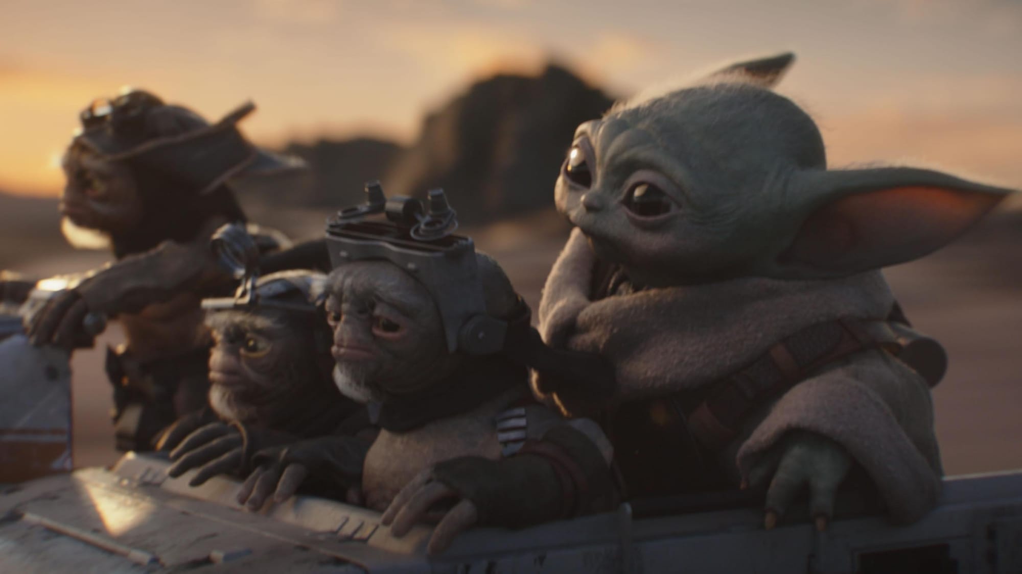 Three Atlassians (small aliens with goggles on their heads) and Grogu (a small Yoda-like creature) in a speeder rushing through the desert.