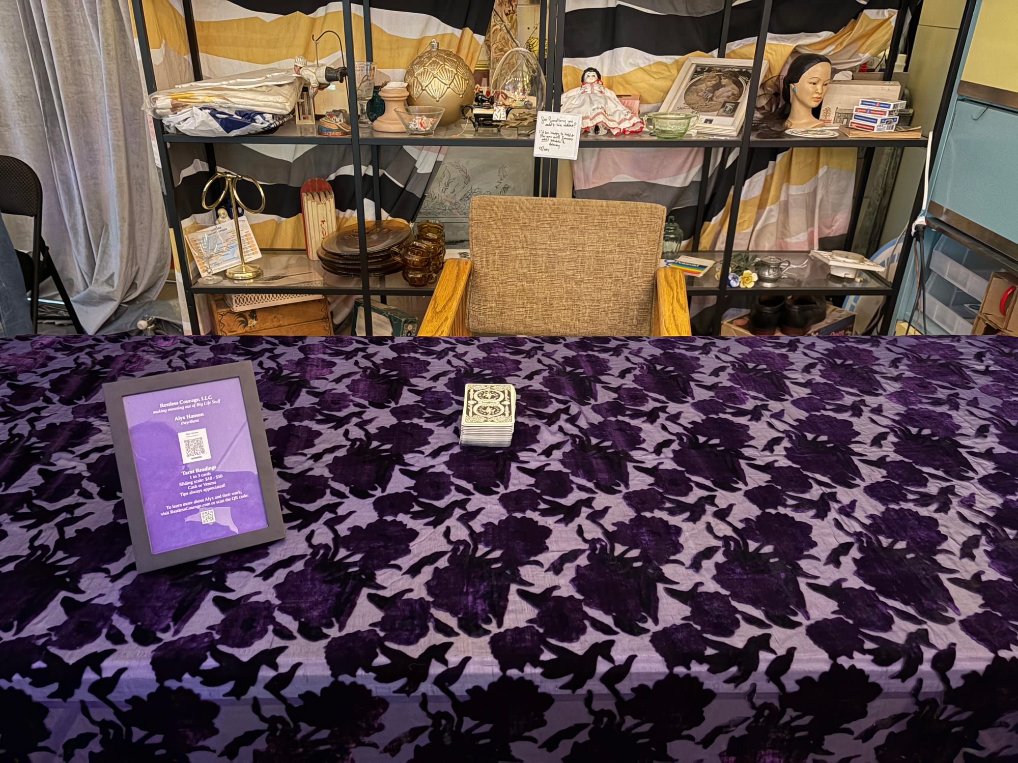 a purple silk cloth with a velvet floral pattern covers a table; there's a purple sign on the left with pricing information and a tarot deck sits in the center of the table, waiting to be used.