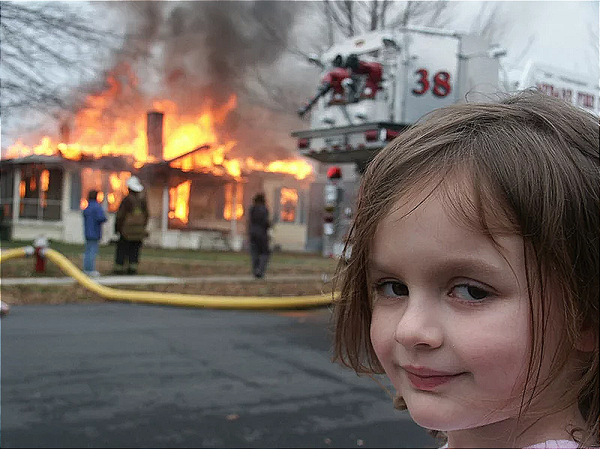 Disaster girl looks at the camera as the house burns