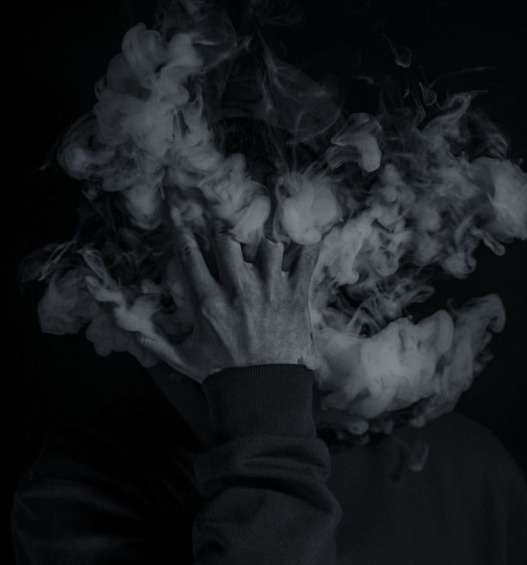 Person with smoke coming from their face and head with a hand obscured by the plumes.
