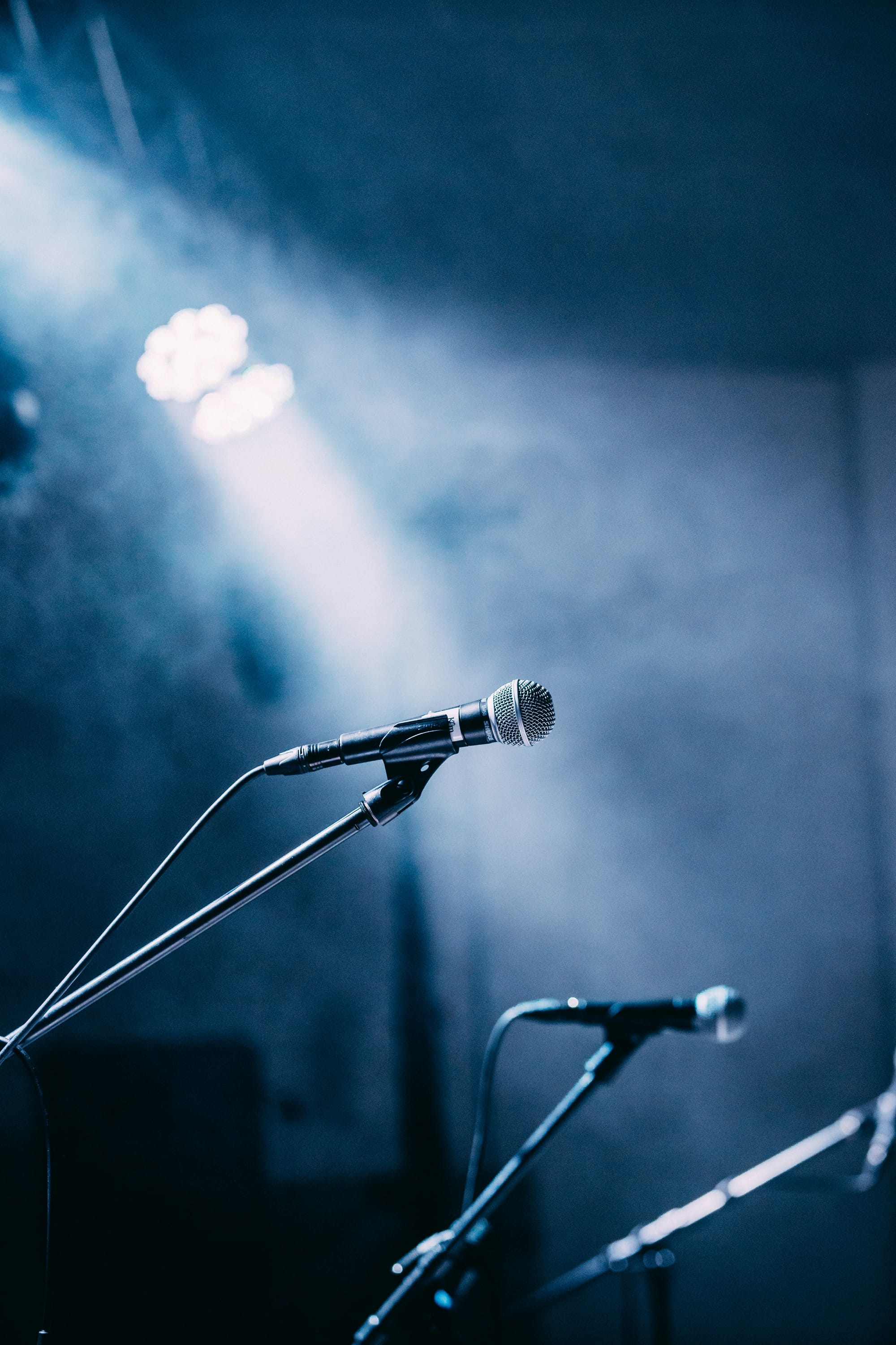 Close-up of a dynamic microphone on stage with dramatic blue lighting and smoke in the background, ready for live performance.