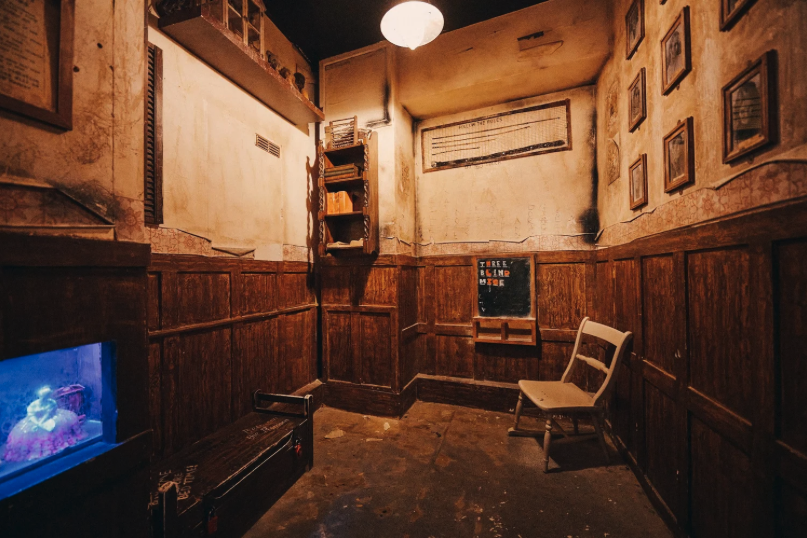 A scene inside an escape room showing a chair, a blackboard and pictures on the wall.