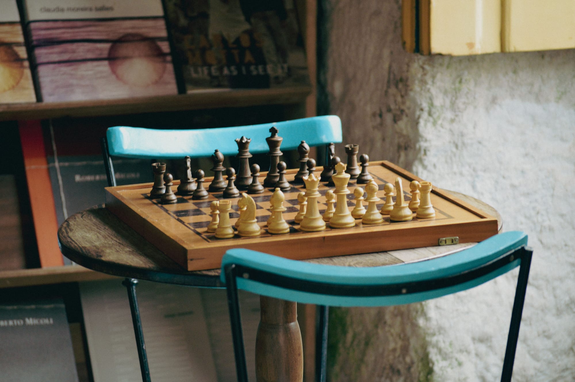 A chess board on a table with two chairs, waiting for people to play it.