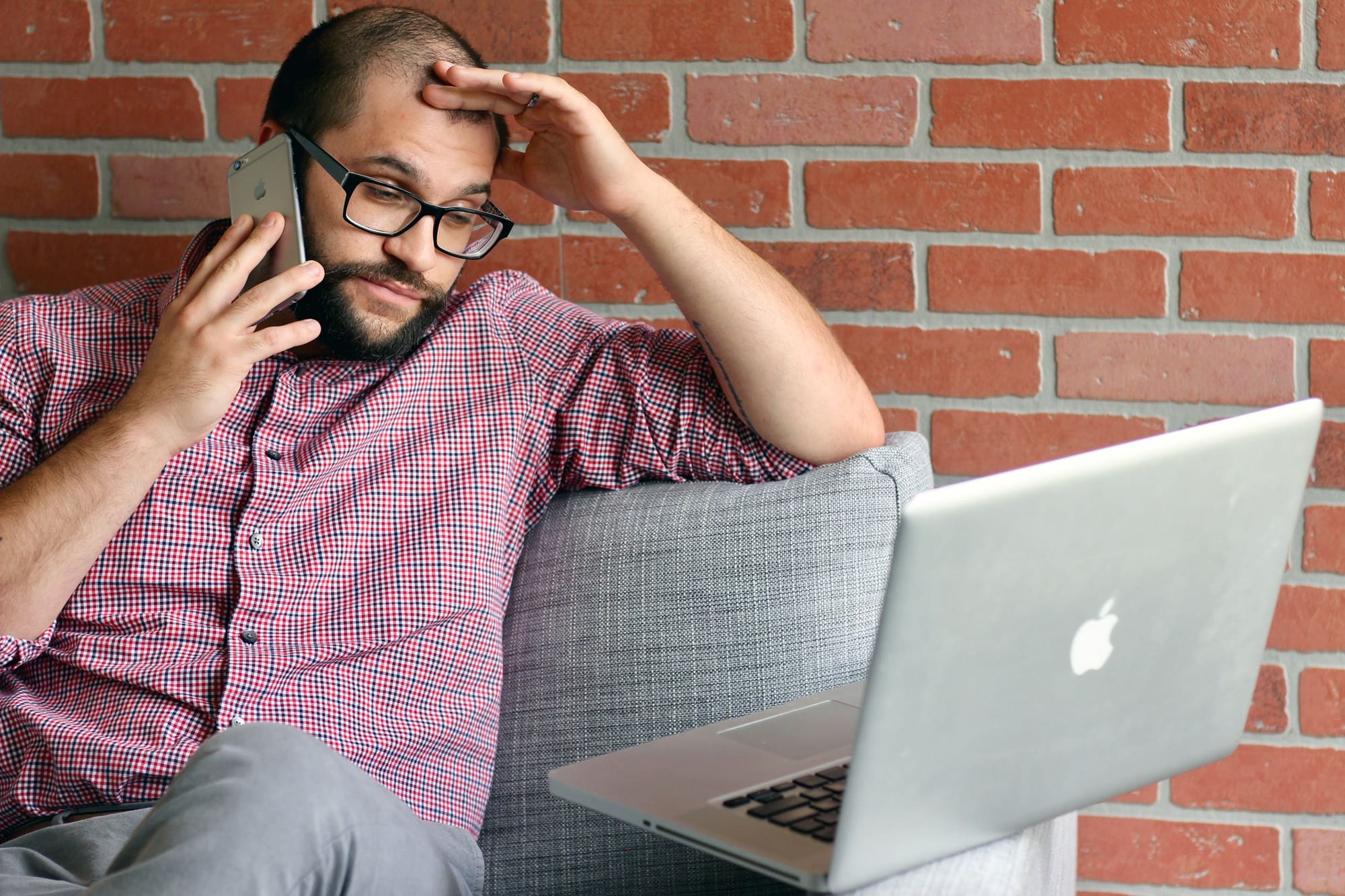 A man on the phone looking at a laptop screen with a vaguely forlorn expression.