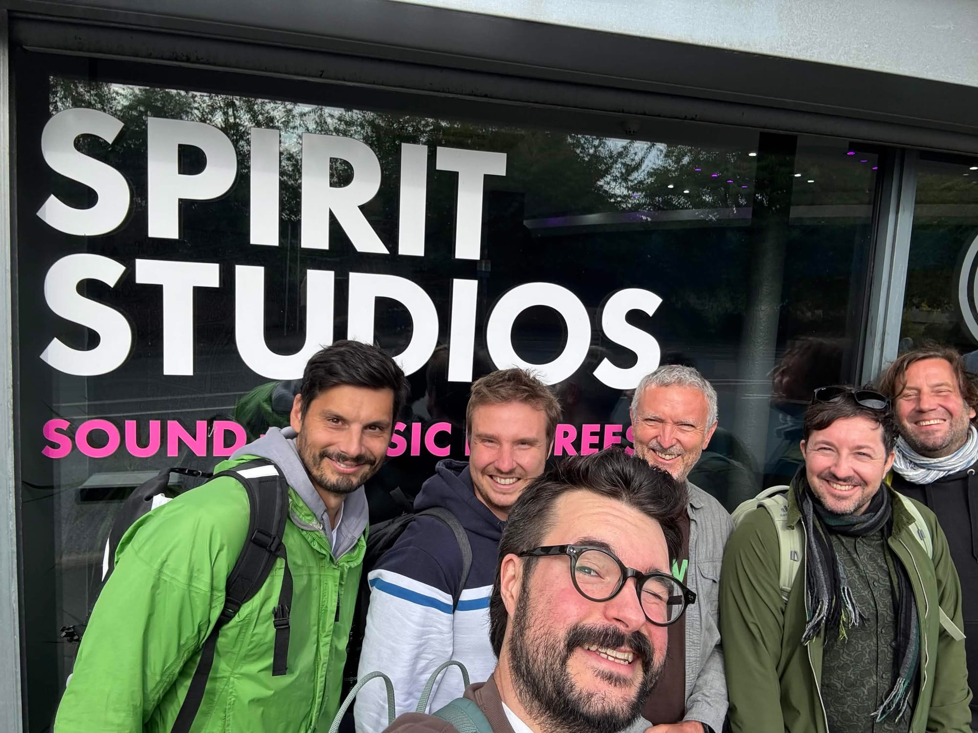 A group of people outside a recording studio smiling taking a selfie.