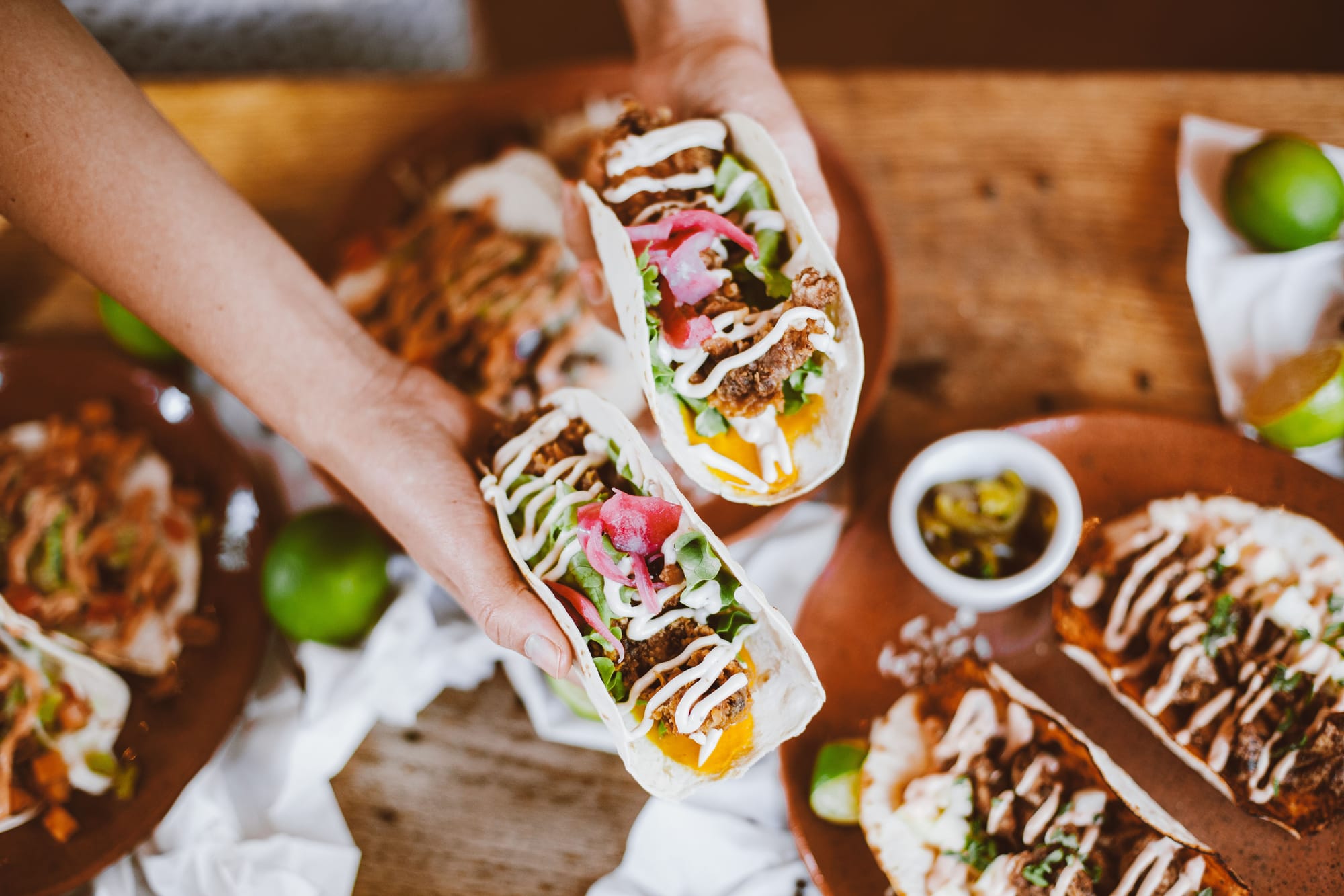 Someone holding out two delicious tacos with colourful fillings.
