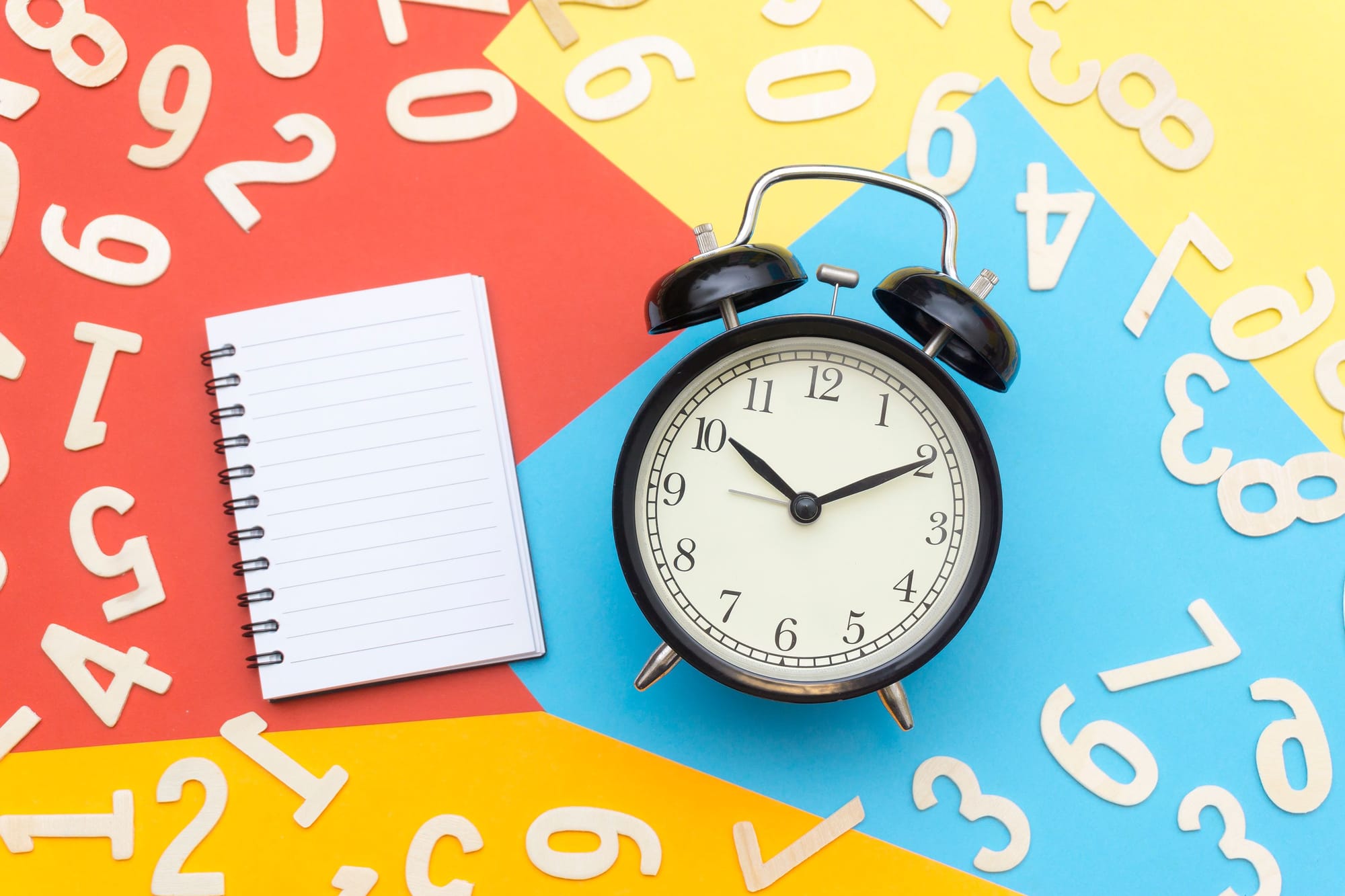 A notepad and alarm clock on a colourful background surrounded by numbers.